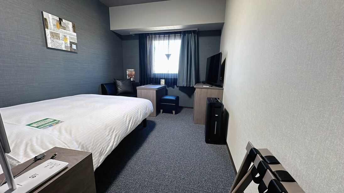 A hotel room with a bed, desk, chair, television, and a small table with a laptop.