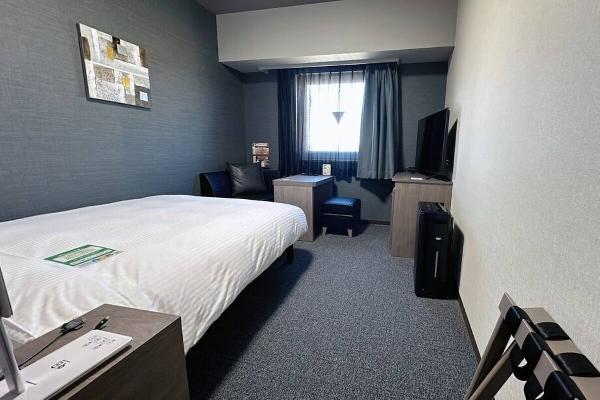 A hotel room with a bed, desk, chair, television, and a small table with a laptop.