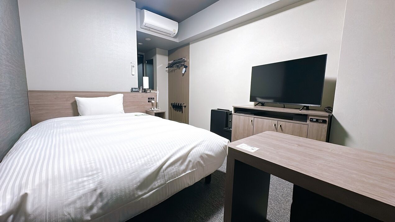 A hotel room with a bed, a TV, a desk, and a wardrobe.