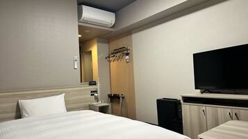 A hotel room with a bed, a TV, a wardrobe, and an air conditioning unit.