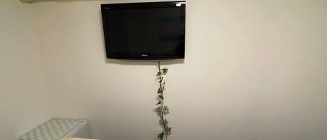 A hotel room with two beds, a flat-screen TV, an air conditioning unit, and a small table.