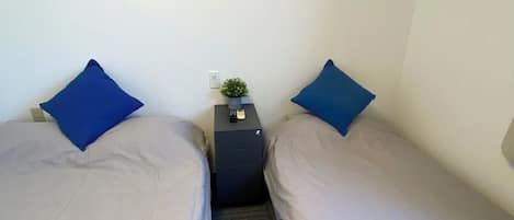 Une chambre d’hôtel avec deux lits, une table de chevet ornée d’une plante et un tableau représentant un coucher de soleil sur l’océan.