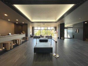 A spacious lobby with a reception desk, seating area, and large windows offering a view of the outdoors. - Hotel Route Inn Numata (Numata)
