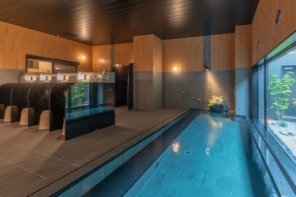 A modern indoor pool area with a long pool, a sauna, and a seating area with a view of the outdoors. - Hotel Route Inn Numata (Numata)