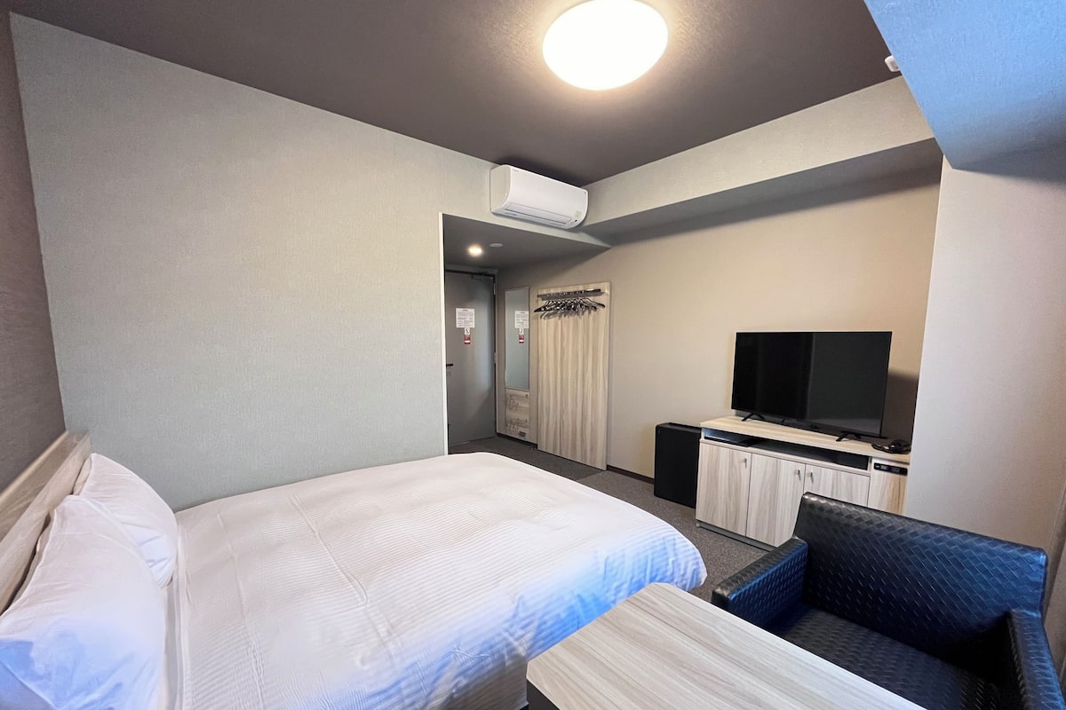 A hotel room with a bed, a small table, a TV, and a seating area.