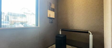 A corner of a hallway with a window, a black trash bin, and a wall-mounted sign.
