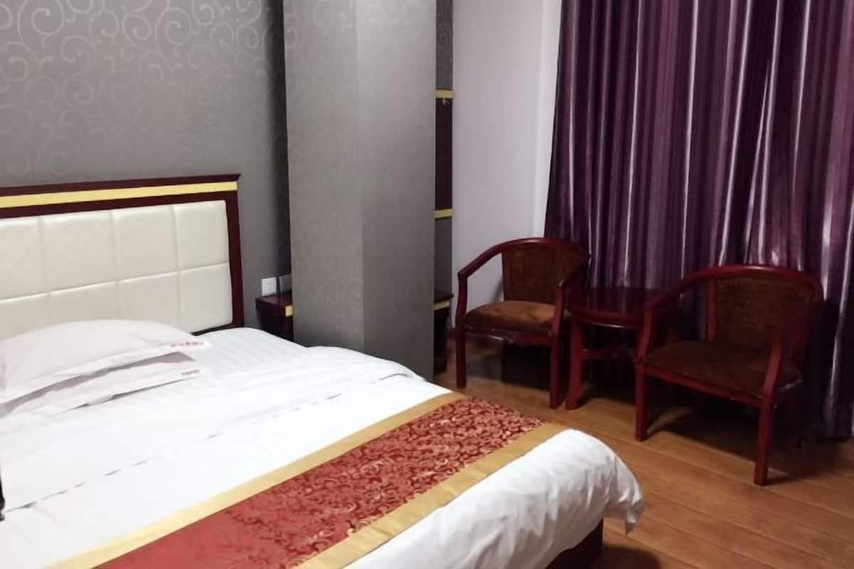 Une chambre d’hôtel avec un lit, deux chaises en bois, une moquette rouge et un rideau.