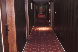 A long, narrow hallway with a patterned carpet, wooden walls, and doors on both sides.