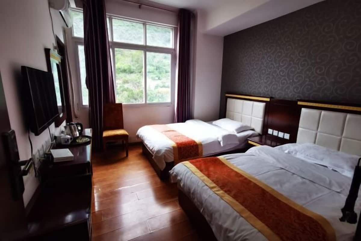 Une chambre d’hôtel avec deux lits, un bureau avec une chaise, une fenêtre avec des rideaux et un téléviseur fixé au mur.