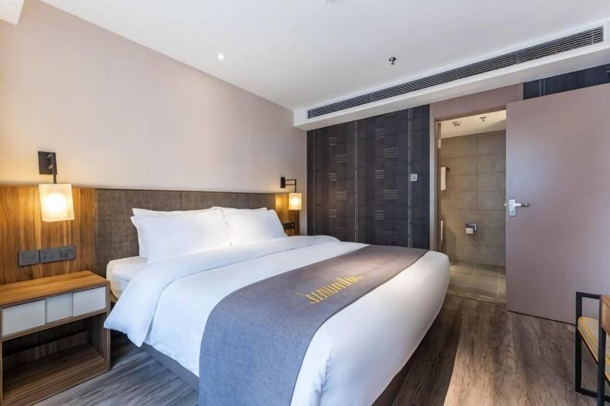 A hotel room with a bed, bedside table, wall-mounted lamp, and a wardrobe.