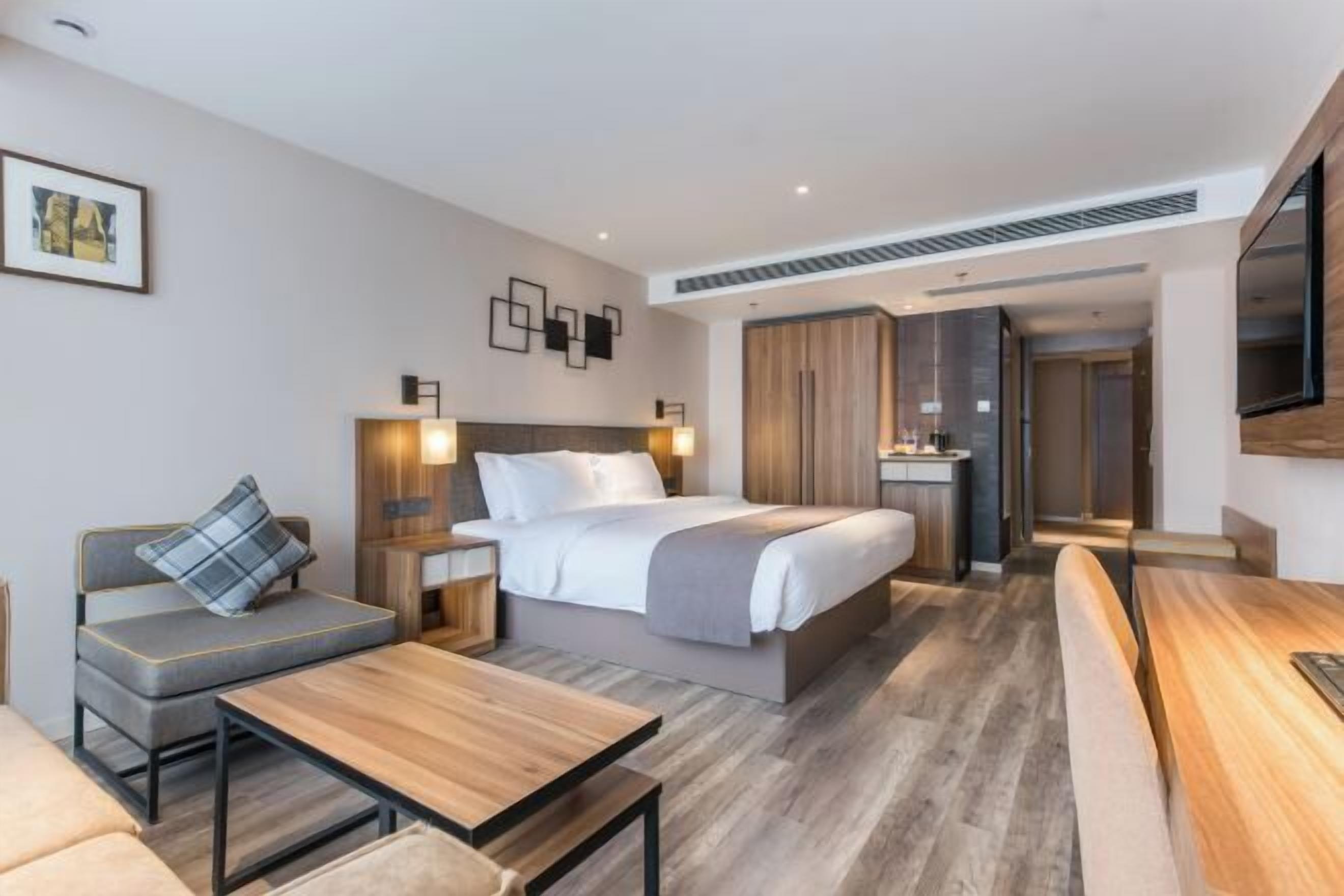 A modern hotel room with a bed, sofa, bedside tables, and a TV.