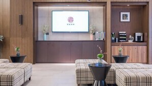 Un moderno vestíbulo de hotel con un mostrador de recepción, una gran pantalla mostrando el logotipo del hotel y una estación de café.
