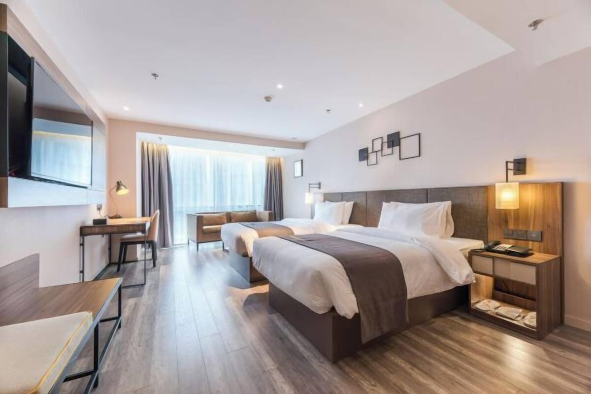 A modern hotel room with a large bed, a desk, a chair, and a TV mounted on the wall.