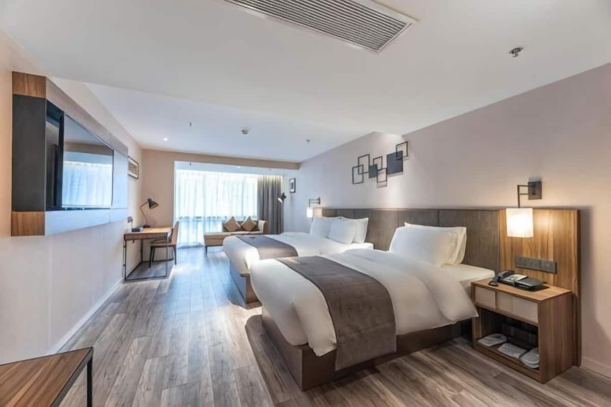 A hotel room with two beds, a desk, a chair, a TV, and a window.