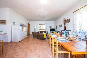 Amplia sala de estar con una mesa de comedor preparada para cuatro, una cocina con refrigerador y una zona de estar con sofás.