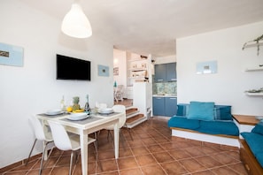 Ein modernes Wohnzimmer mit Essbereich, einem an der Wand befestigten Fernseher und einem blauen Sofa.