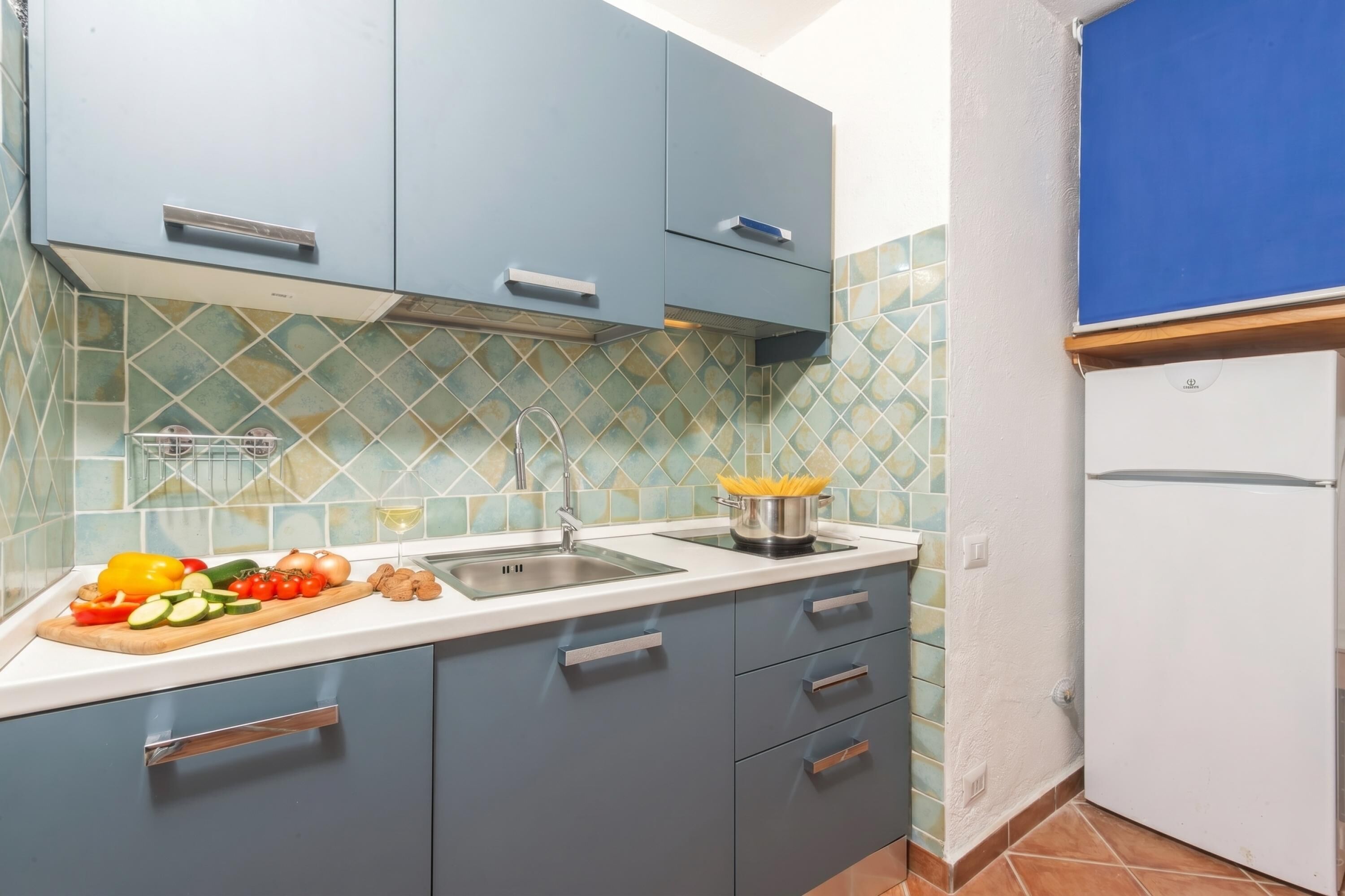 A kitchen with blue cabinets, a white countertop, and a tiled backsplash.