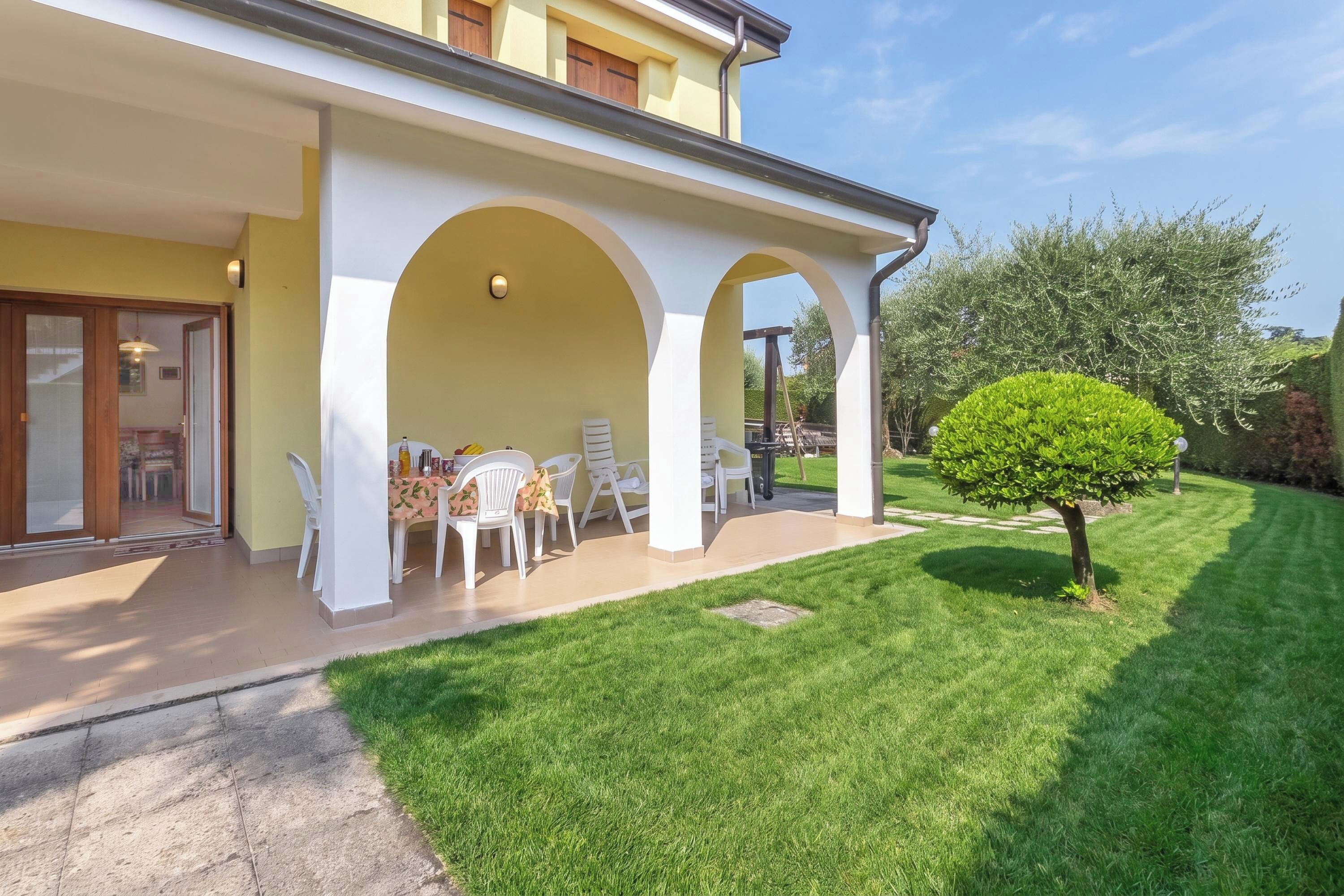 Une maison avec un patio couvert, une pelouse et un petit arbre.