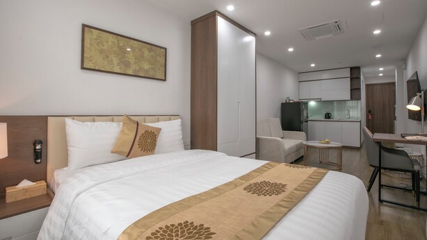 Ein modernes Hotelzimmer mit einem großen Bett, einem Schreibtisch, einem Sessel, einem kleinen Tisch, einem Spiegel und einer Küchenzeile.