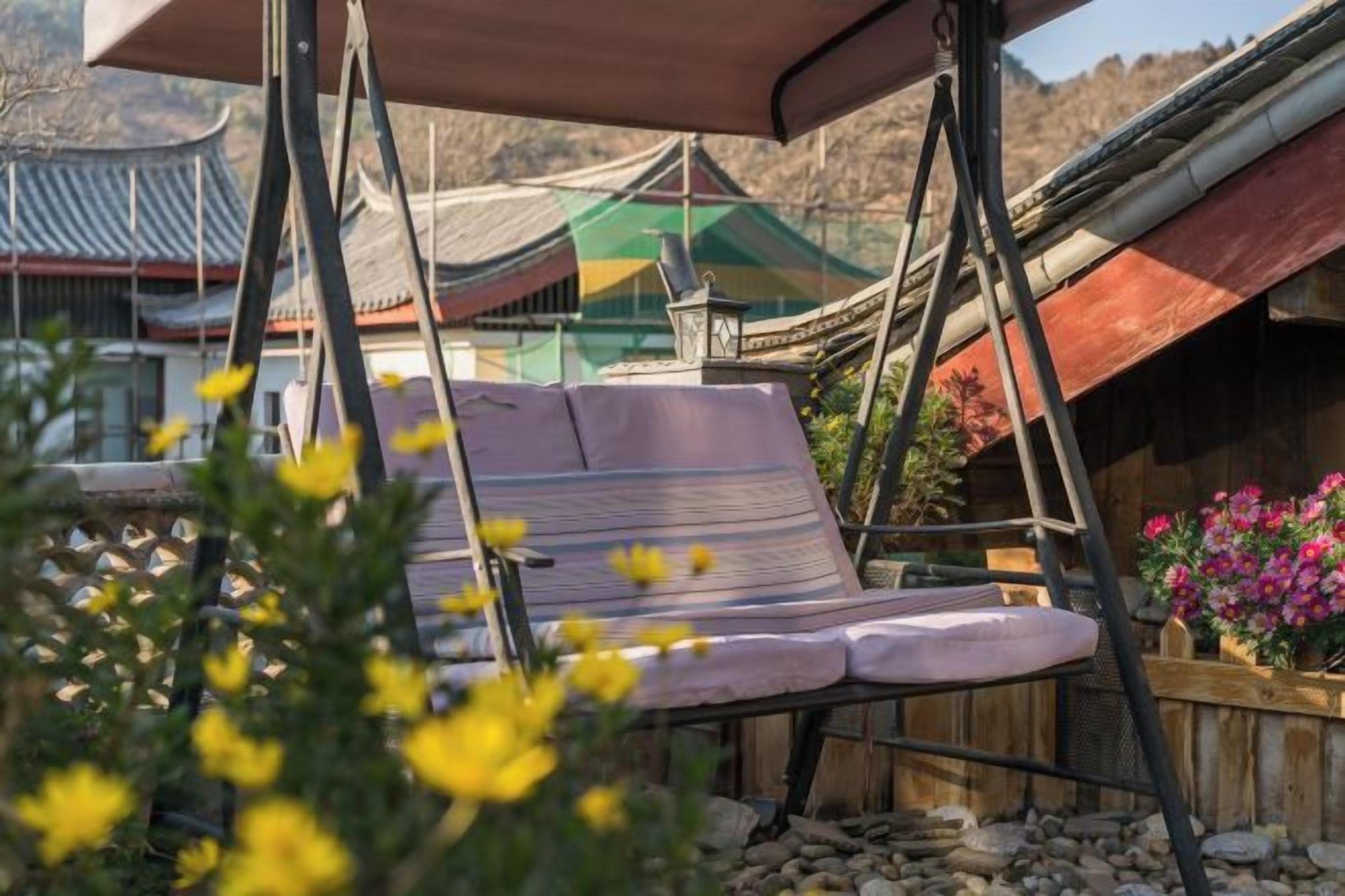Une structure traditionnelle en bois, dotée d’un toit en pente, d’une chaise suspendue et d’un banc en bois.