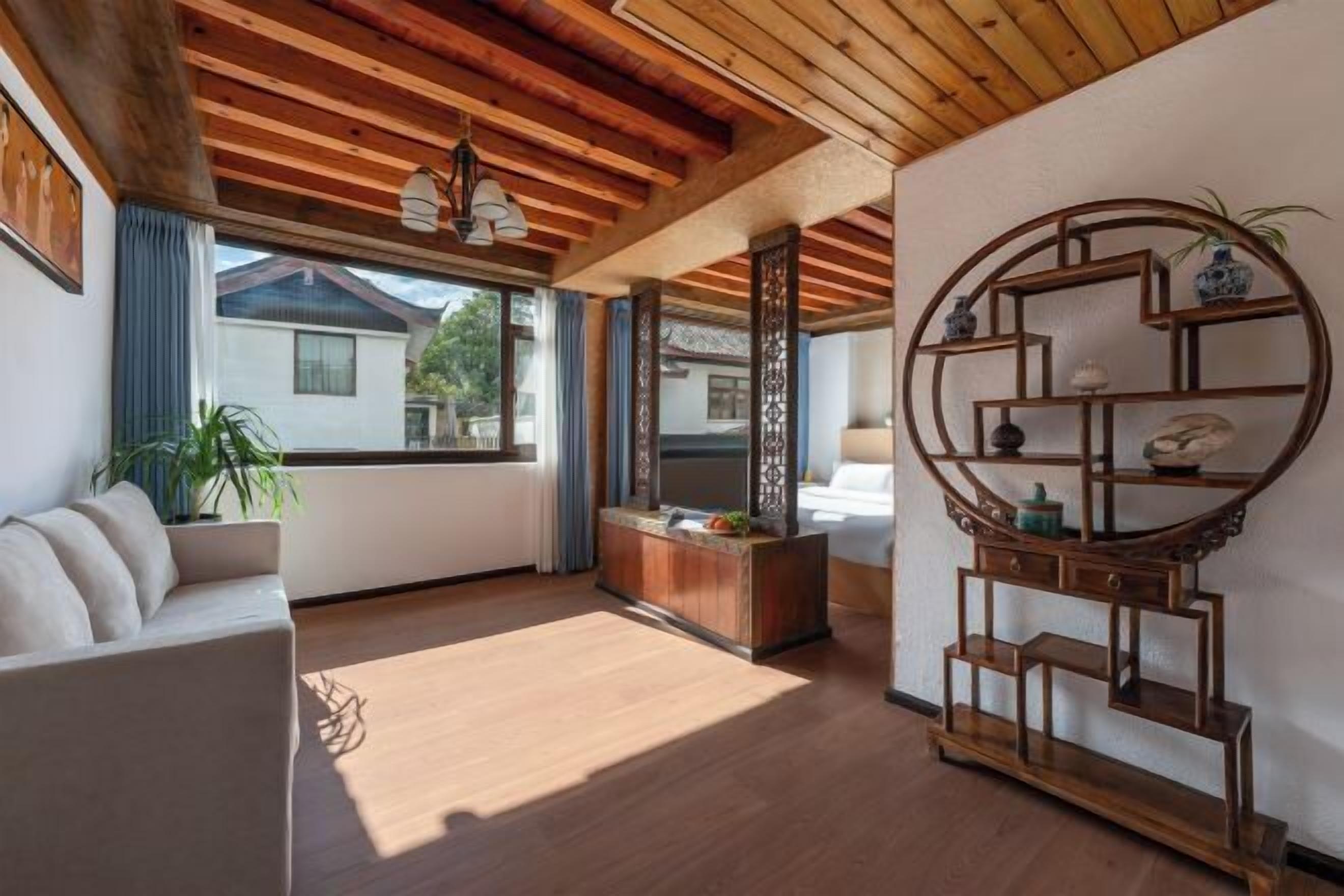 Sala de estar com teto de madeira, sofá, mesa de centro, estante de madeira decorativa e vista para o exterior.