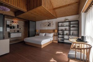 Um quarto com cama, mesas de cabeceira, uma pequena escrivaninha, uma cadeira, estante de livros e um espaço de cozinha.