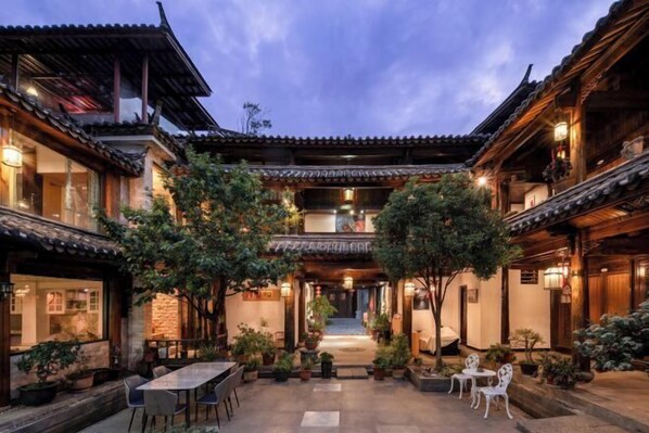 A traditional courtyard with a dining area, potted plants, and a central staircase. - Nalan Ge homestay (Lijiang)