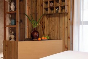 Uma prateleira de madeira com objetos decorativos, um vaso com plantas verdes e uma tigela de frutas.