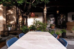 An outdoor dining area with a table and chairs, surrounded by potted plants and a tree.