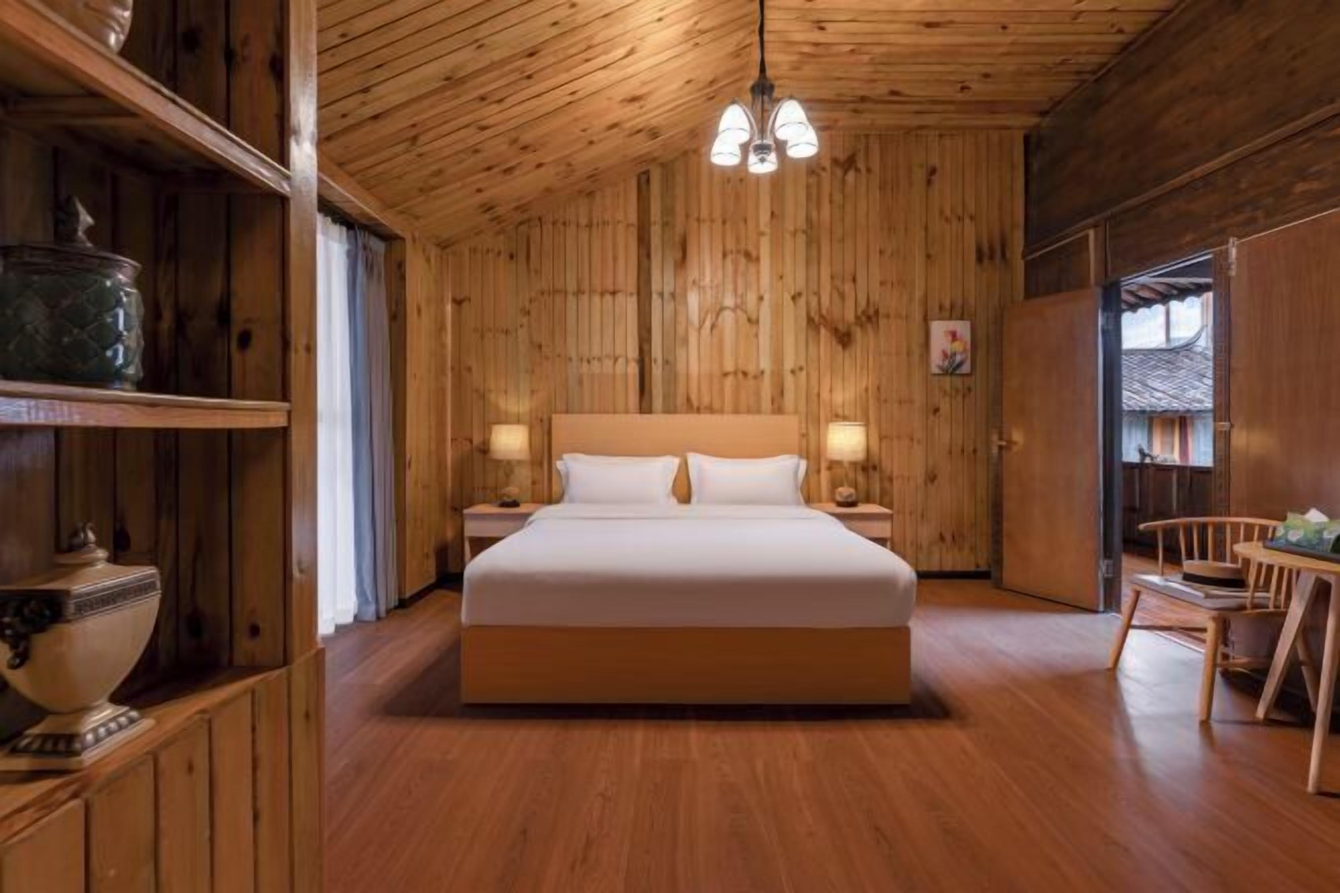 Quarto de madeira com cama, mesas de cabeceira e luminária pendente.
