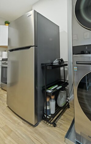 A kitchen with a stainless steel refrigerator, a built-in oven, and a black storage cart with bottles.