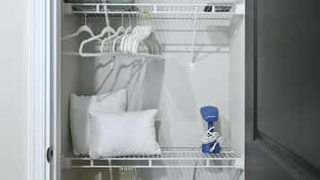 Een kleine opbergruimte met planken voor opgevouwen kleding, een kledingroede en een klein bankje met een opbergbak.