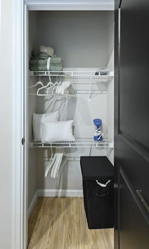 A compact storage area with shelves for folded clothes, a hanging rack for garments, and a small bench with a storage bin.