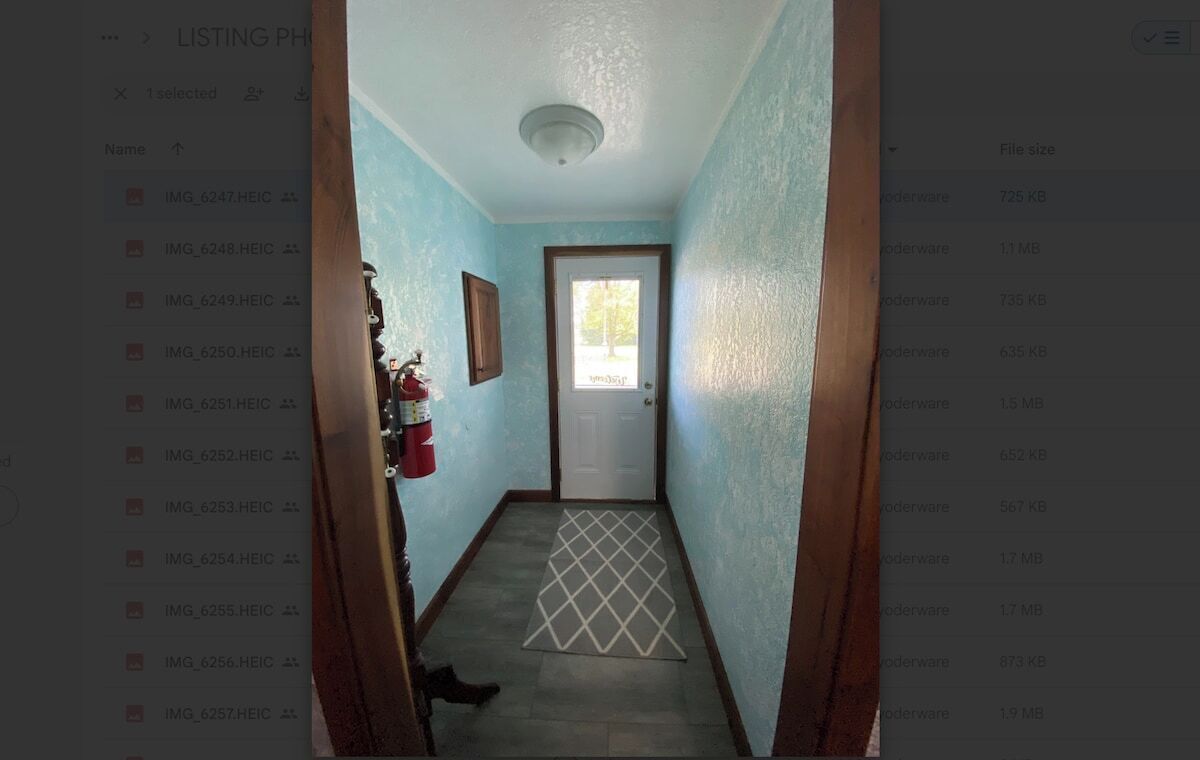 A narrow hallway with a door at the end, a fire extinguisher on the wall, and a patterned rug on the floor.