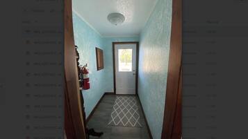 A narrow hallway with a door at the end, a fire extinguisher on the wall, and a patterned rug on the floor.