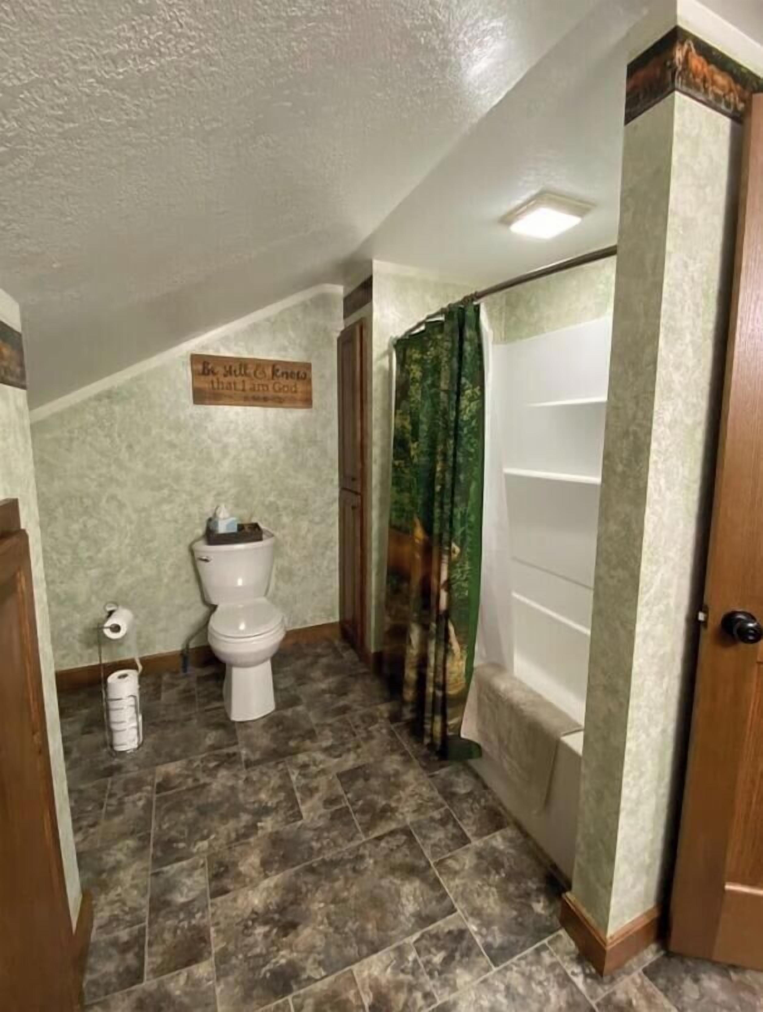 Un bagno con il water, una tenda per la doccia e un cartello a parete.