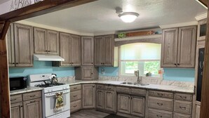A kitchen with wooden cabinets, a stove, a microwave, and a sink. - Peaceful Meadows - Peaceful Meadows (Flat Rock)
