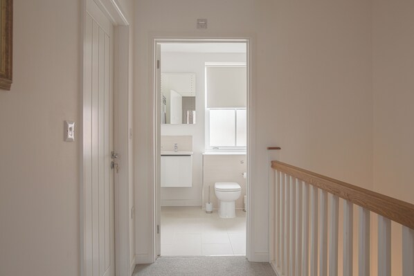 Pasillo que conduce a un baño con inodoro, lavabo y espejo.
