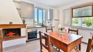 Una cocina moderna con armarios blancos, horno empotrado y comedor con mesa y sillas de madera.