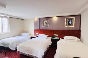 Una habitación de hotel con tres camas individuales, un cabecero de madera, una mesita de noche con teléfono y un cuadro en la pared.