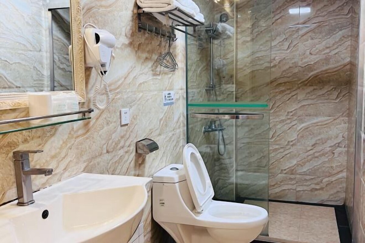 A bathroom with a marble wall, a glass shower enclosure, a sink, a toilet, and a hairdryer.
