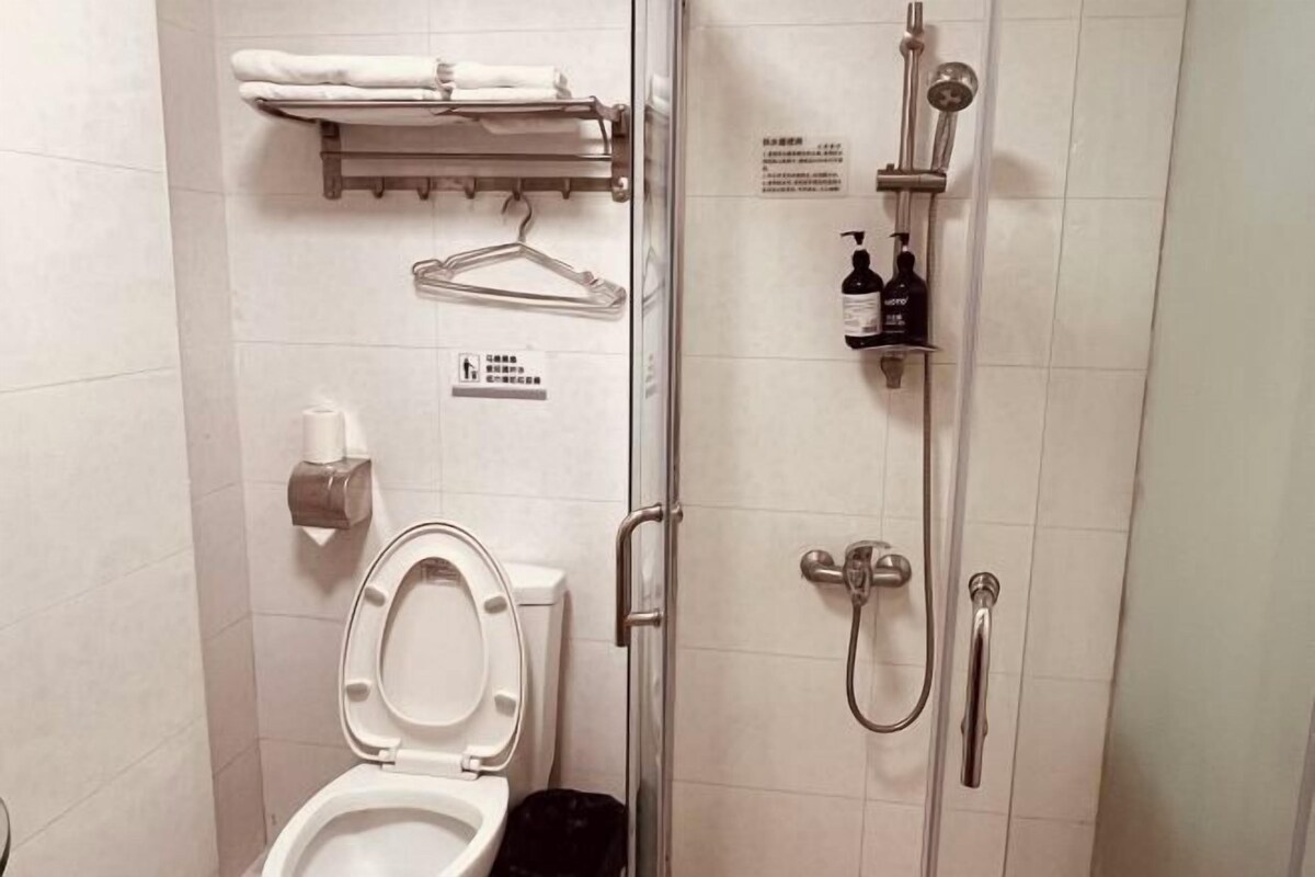 A bathroom with a toilet, a shower, a towel rack, and a hand dryer.
