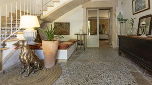 Ein geräumiges Foyer mit einer Treppe, einer großen Kübelpflanze, einer Hundestatue und einem Essbereich im Hintergrund.