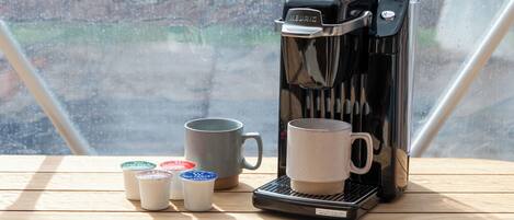 Una máquina de café Keurig sobre una mesa de madera con una taza gris y tres tazas pequeñas con tapa.