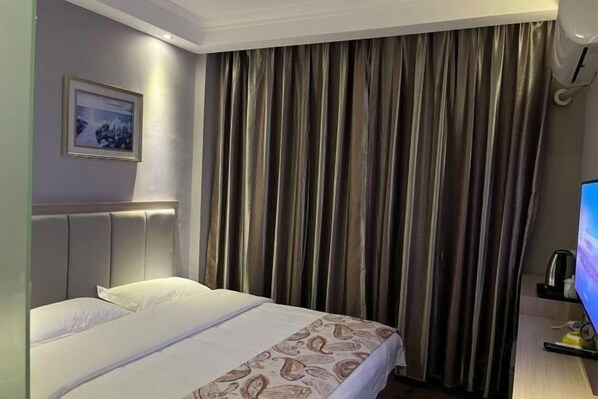 Habitación de hotel con cama, televisor y un amplio ventanal con cortinas.