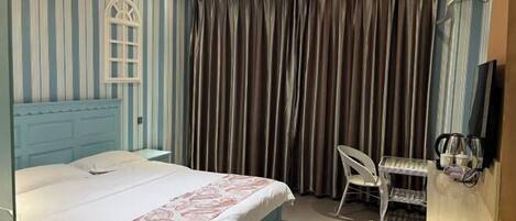 A hotel room with a bed, a desk with a chair, a TV, and curtains.