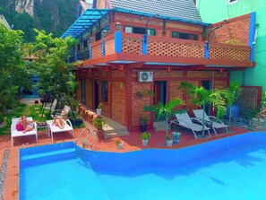 A two-story building with a swimming pool, outdoor lounge chairs, and potted plants. - Vu's Homestay Phong Nha (Phong Nha)