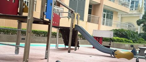 A playground with a red and yellow ride-on toy, a slide, and a climbing structure.