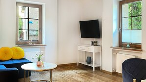 A modern living room with a sofa, a coffee table, a TV, and a window with a view of greenery. - Warszauera 11/1 (Kraków)