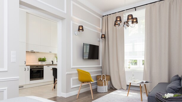 A modern living room with a sofa, a yellow chair, a TV, and a window with curtains.